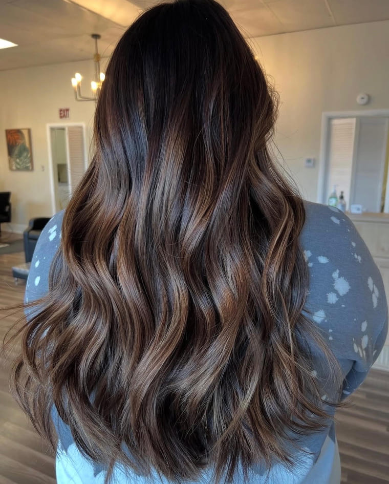 Dark dimensional brunette with caramel highlights on long waves, colored by Amanda